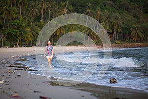 Young mixed-race woman walks along a polluted tropical beach.