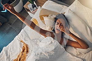 A young mixed race woman yawning and stretching while lying in bed. An attractive Hispanic female waking up from a her