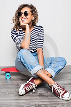 Young mixed raced girl sitting on cruiserboard sitting on floor isolated on white background.