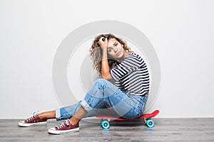 Young mixed raced girl sitting on cruiserboard sitting on floor on white background.