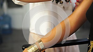 Young model putting on her hand golden bracelets while a makeup artist is preparing her for a fashion show and applying