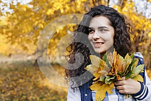 Young model standing in autumn park and holding in hands bunch of leaves