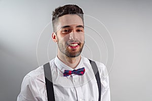 Young model in white shirt, suspenders, bow tie, piercings and fledgling beard