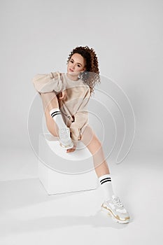 Young model woman with long sexy legs and perfect slim body wearing a grey sweatshirt and trendy sneakers posing over