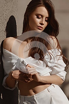Young model woman with perfect slim body in white trendy outfit posing outdoors on the summer day