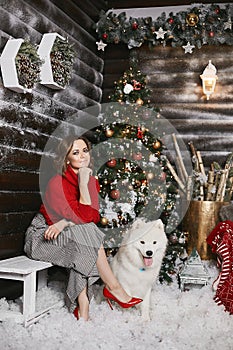 Young model woman in red shoes, plaid skirt and red sweater posing with fluffy Samoyed dog against background of New