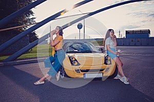 Young models are eating hamburgers and holding beverages in paper cups while leaning on the hood of yellow car. Fast