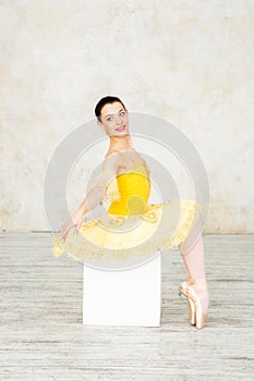 Young modern ballerina in yellow dress posing in the light ballet room