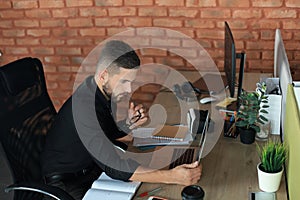 Young modern business man analyzing data using laptop while working in the office