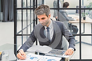 Young modern business man analyzing data using laptop while working in the office with collegues on the background.