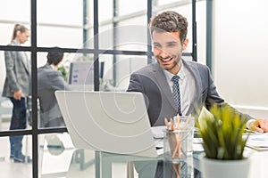 Young modern business man analyzing data using laptop while working in the office with collegues on the background.