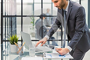 Young modern business man analyzing data using laptop while working in the office with collegues on the background.