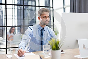 Young modern business man working using computer with collegues on the background while sitting in the office.