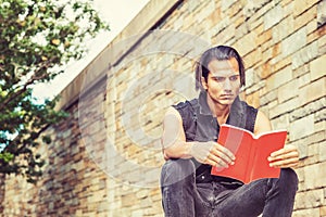 Young Modern East Indian American Man reading red book outside in New York City