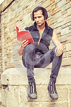 Young Modern East Indian American Man reading red book outside in New York City