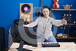 Young modern girl with blue hair at music studio wearing headphones looking at the camera smiling with open arms for hug