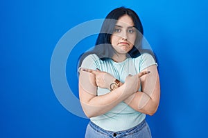 Young modern girl with blue hair standing over blue background pointing to both sides with fingers, different direction disagree