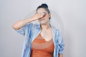 Young modern girl with blue hair standing over white background covering eyes with hand, looking serious and sad