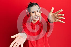 Young modern girl wearing gym clothes and using headphones looking at the camera smiling with open arms for hug