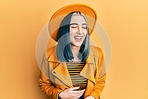 Young modern girl wearing yellow hat and leather jacket smiling and laughing hard out loud because funny crazy joke with hands on