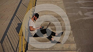 Young modern happy man without shoes, sitting on urban stairs, using laptop, wearing black cap and socks