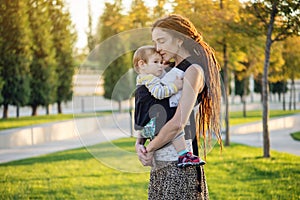 Young modern happy mom with baby son walking in Sunny Park. The concept of the joy of motherhood