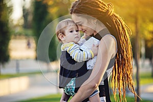 Young modern happy mom with baby son walking in Sunny Park. The concept of the joy of motherhood