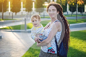 Young modern happy mom with baby son walking in Sunny Park. Concept of the joy of motherhood and autumn mood