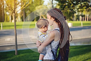 Young modern happy mom with baby son walking in Sunny Park. Concept of the joy of motherhood and autumn mood