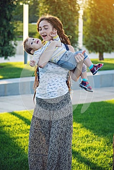 Young modern happy mom with baby son walking in Sunny Park. Joy of motherhood and autumn mood