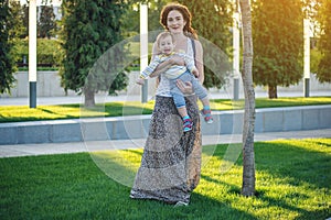 Young modern happy mom with baby son walking in Sunny Park. Joy of motherhood and autumn mood