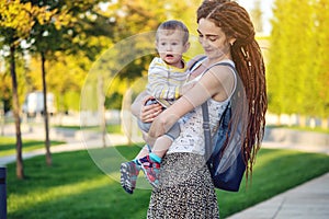 Young modern happy mom with baby son walking in Sunny Park. Joy of motherhood and autumn mood