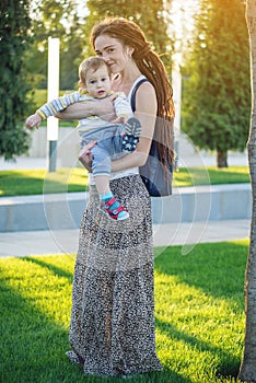 Young modern happy mom with baby son walking in Sunny Park. Joy of motherhood and autumn mood