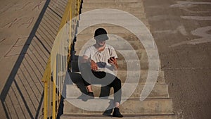 Young modern man in socks, sitting on urban stairs, making selfie with smartphone.