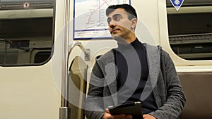 A young modern man with a tablet sitting in a train carriage. Media. Portrait of a handsome man with black hair wearing