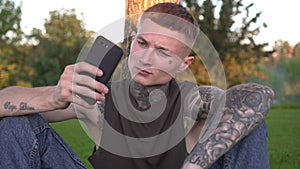 Young modern man in tattoos uses a smartphone in the park. Youth subculture