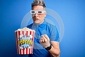 Young modern man watching cinema movie wearing 3d glasses and eating popcorn annoyed and frustrated shouting with anger, crazy and