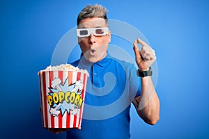 Young modern man watching cinema movie wearing 3d glasses and eating popcorn scared in shock with a surprise face, afraid and