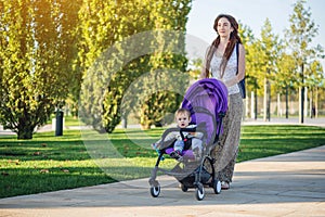 Young modern mom with baby son in stroller walking in Sunny Park. Concept of the joy of motherhood and autumn mood