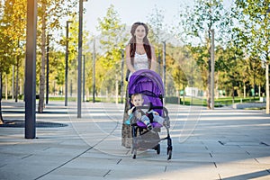 Young modern mom with baby son in stroller walking in Sunny Park. Concept of the joy of motherhood and autumn mood