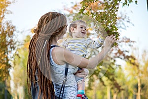 Young modern mom with baby son walking in Sunny Park. Concept of the joy of motherhood