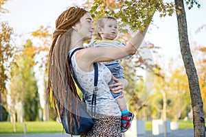 Young modern mom with baby son walking in Sunny Park. Concept of the joy of motherhood