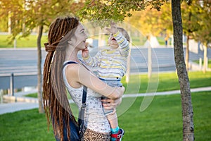 Young modern mom with baby son walking in Sunny Park. Concept of the joy of motherhood