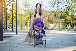 Young modern mother with baby son in stroller walking in Sunny Park. Concept of the joy of motherhood and autumn mood