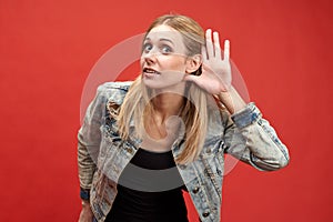 Young modern stylish woman picturesquely puts her hand to her ear in a sign of listening attentively or eavesdropping.