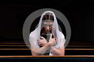 A young modest girl with a handkerchief on her head and a bible in her hands is sitting in church and praying. The concept of