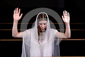 A young modest girl with a handkerchief on her head is sitting in church and praying. The concept of religion, prayer, worship