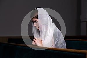 A young modest girl with a handkerchief on her head is sitting in church and praying. The concept of religion, prayer, worship