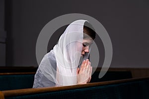 A young modest girl with a handkerchief on her head is sitting in church and praying. The concept of religion, prayer, worship