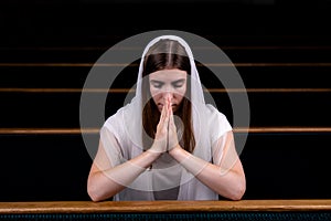 A young modest girl with a handkerchief on her head is sitting in church and praying. The concept of religion, prayer, worship
